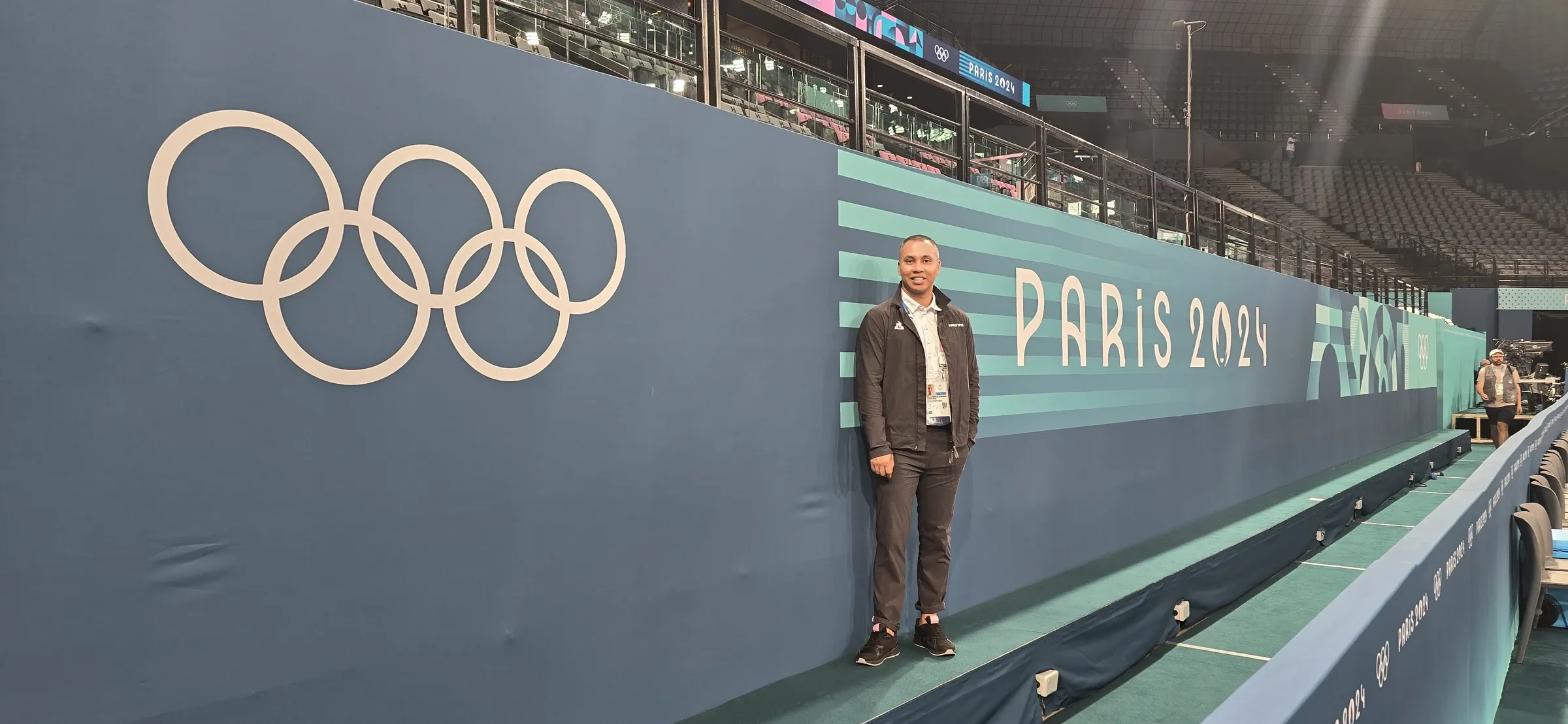 Arturo Padilla de pie junto a los aros olímpicos en la arena de gimnasia de París 2024